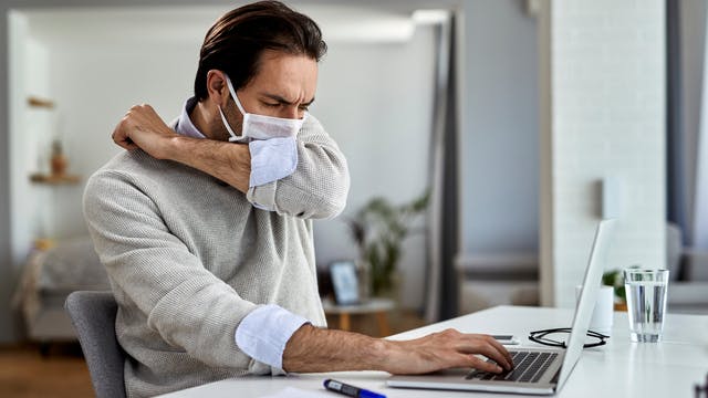 Man wearing face mask coughing into arm