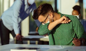 Man coughing into arm while wearing face mask