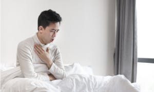 Man sitting on a bed while coughing and holding his chest