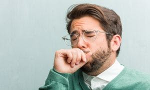 A man has a productive green phlegm sputum cough into his hand with his eyes closed as though he is experiencing discomfort.