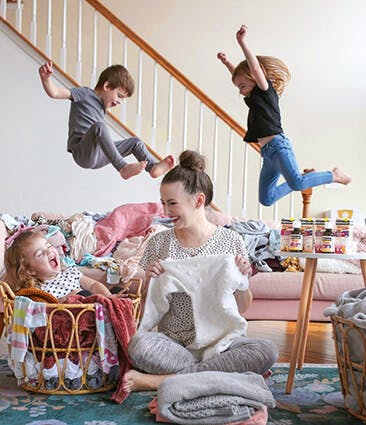 Two kids jumping on sofa behind a woman laughing with child on floor