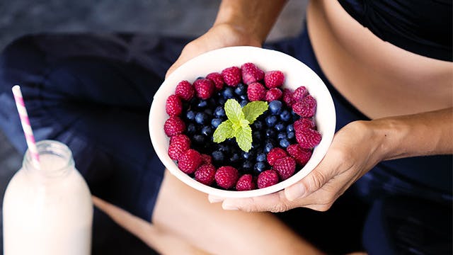 Egy nő egy tál gyümölcsöt tart a kezében, mellette egy üveg tej.