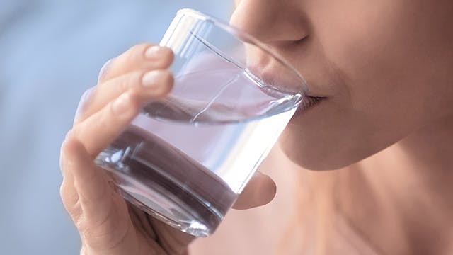 Közeli képkivágás egy nőről, szomjas, kezében egy pohár víz, a víz megakadályozza a dehidratáltságot