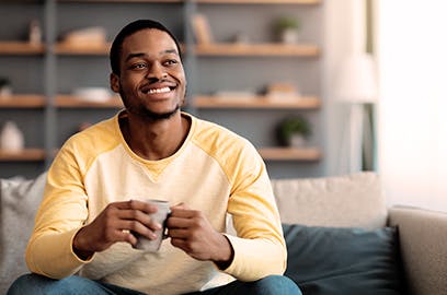 A man is sitting on a sofa in the living room with a mug in his hand, he is smiling