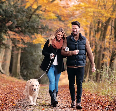 A man and woman are walking down a forest path with a dog on a leash