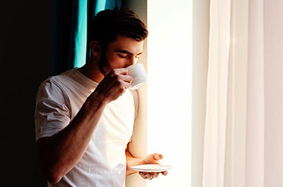 Man drinking cup of coffee next to a window