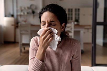 A lady is sneezing into a tissue