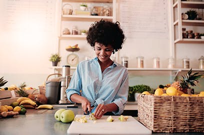 A woman standing in a kitchen is chopping apples on a board.