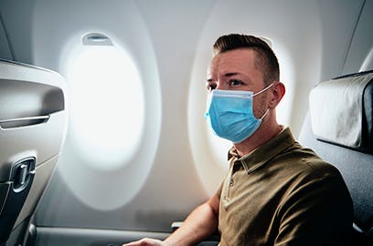 A man sitting on an airplane is wearing a mask