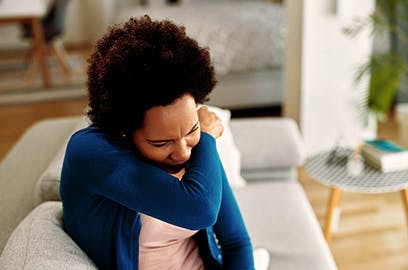 A woman is sitting and coughing into her elbow