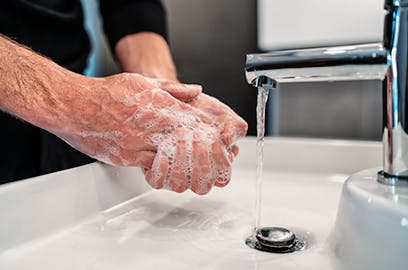 A man with soapy hands rinsing them under running water