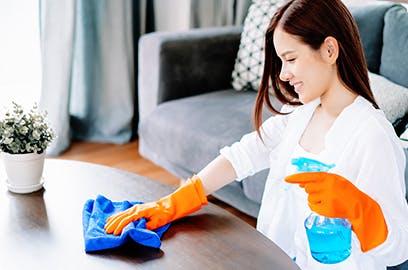 Woman cleaning kitchen table with orange gloves and disinfecting spray