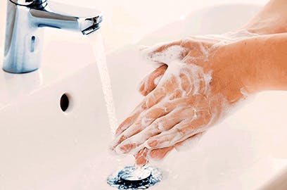 A person with soapy hands is rinsing them under a running tap