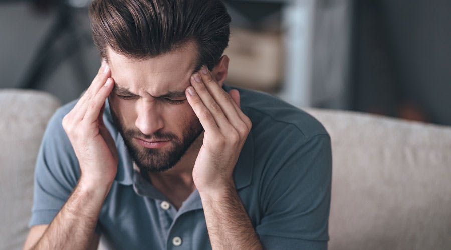 A man is sitting and holding his hands to his head in pain