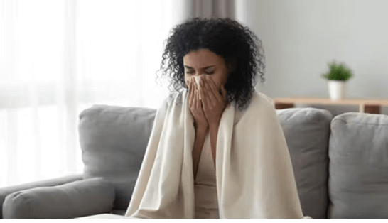 Woman sneezing into tissue with blanket around her shoulders