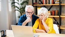 elderly couple looking at computer screen with confused expressions