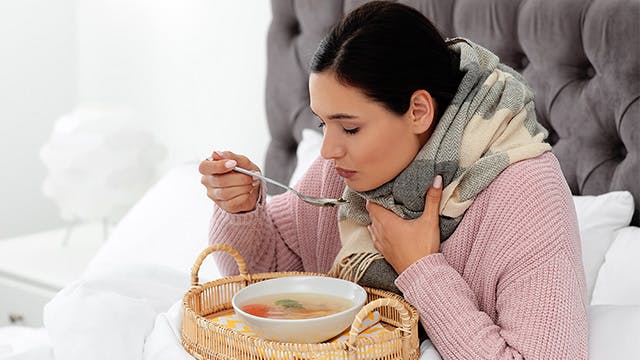 A woman is sitting in bed eating soup 