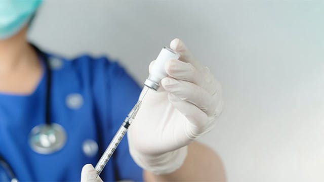 Person in hospital scrubs and mask filling a vaccine needle from a bottle