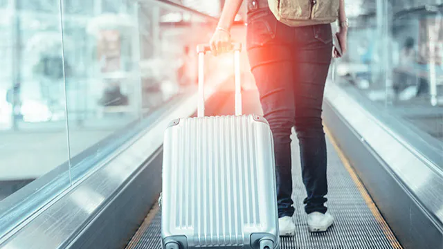 Person pulling a silver suitcase in an airport