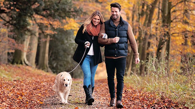 A man and woman are walking down a forest path with a dog on a leash 