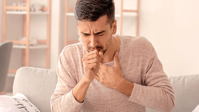 A man is sitting on a sofa and coughing 