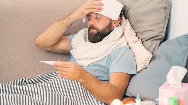 Man on couch with cool forehead compress and thermometer 