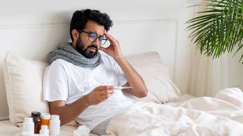 Man in bed looking at thermometer