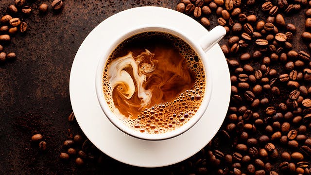 Cup of coffee surrounded by coffee beans 