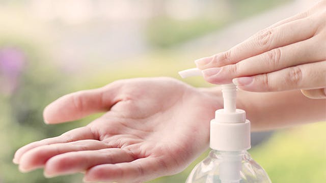Person applying hand sanitizer from a clear bottle to their hands