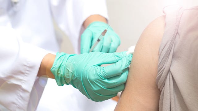 Doctor wearing gloves administering flu shot into arm of patient 