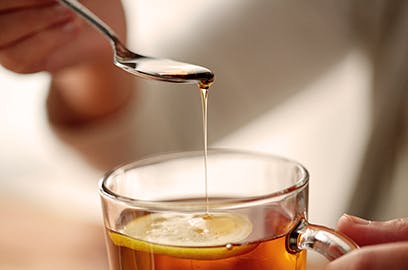 A close up of honey being drizzled into a mug of tea with a lemon slice