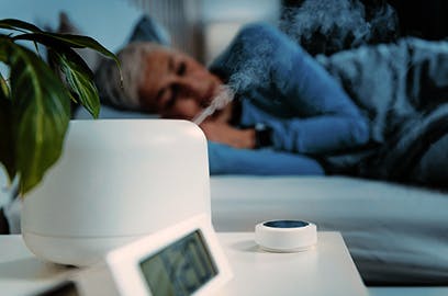 A woman is lying in bed in a darkened room. In the foreground is a humidifier. 