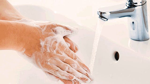 Person washing hands with foaming hand soap under a faucet