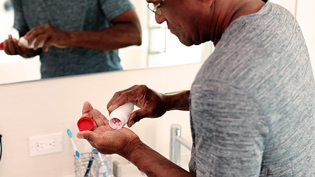 Man in grey shirt pouring supplements into his hand 