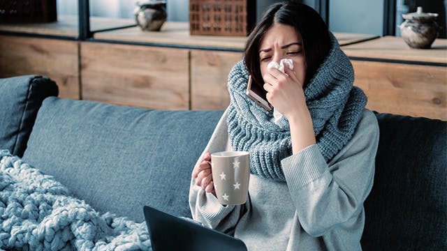 Sick women wearing scarf blows nose on couch 