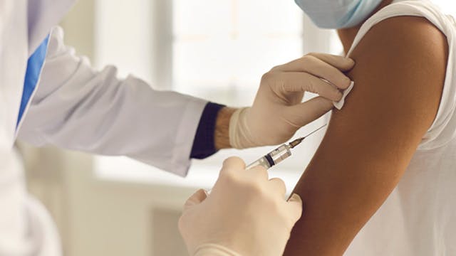 Doctor administering flu shot into arm of masked patient