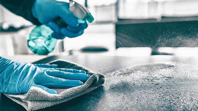 Hands in blue rubber gloves spraying cleaner on a countertop