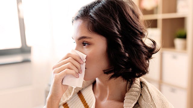 Woman in a striped sweater wiping her nose with a kleenex