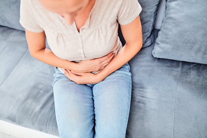 Women with digestive problems sitting on the couch and holding stomach