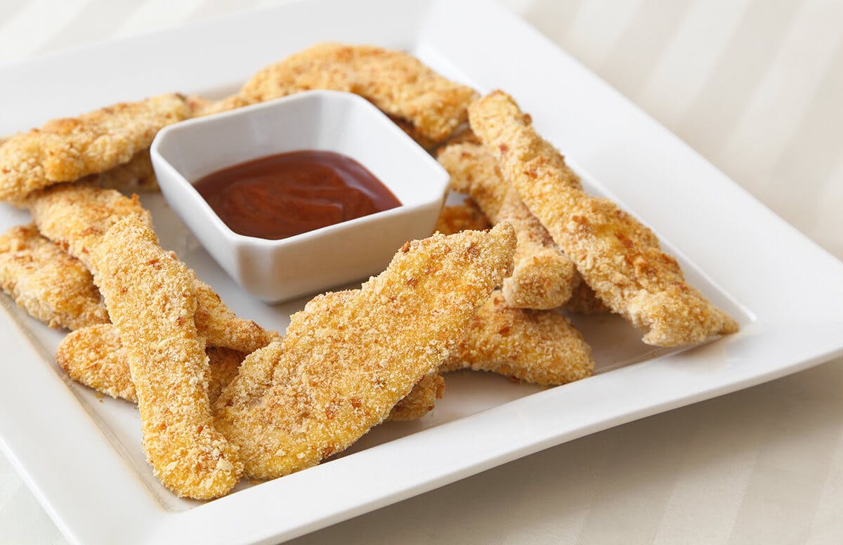 A plate with breaded, baked chicken tenders and a cup of barbecue sauce