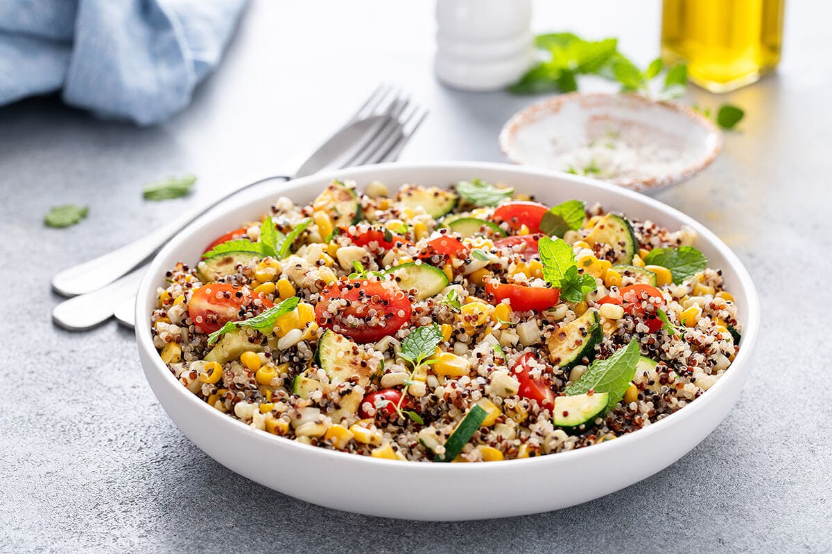 A bowl that has a fresh quinoa salad with tomatoes, corn and zucchini