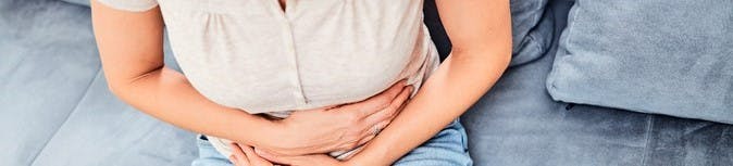 Women with digestive problems sitting on couch and holding stomach