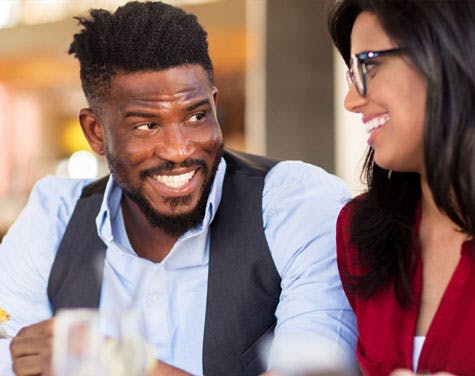 man and woman smiling at each other while having a meal together