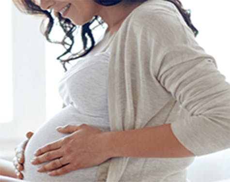 Pregnant woman touching her belly and looking down at it smiling