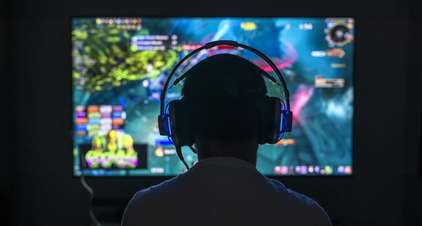 Gamer wearing headphones sitting in front of screen in dark room