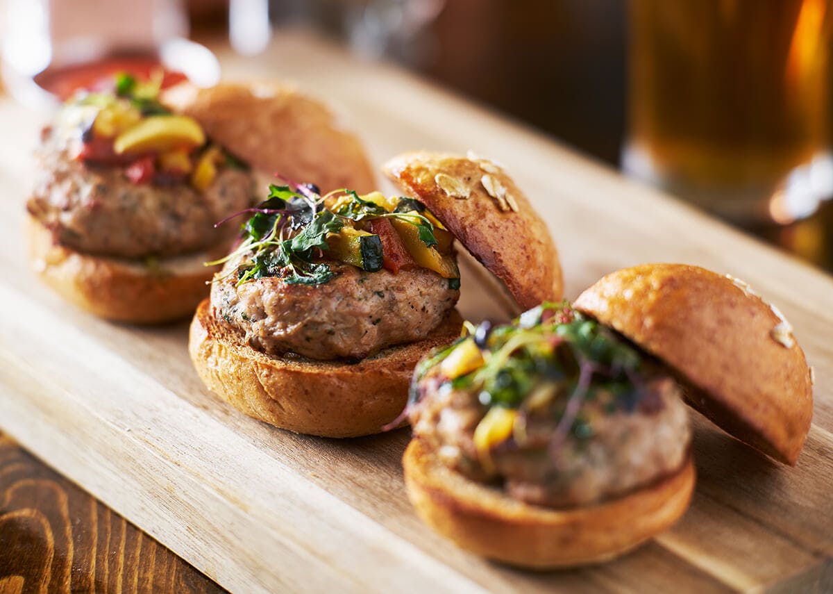 Three turkey sliders topped with roasted vegetables and herbs on a plate