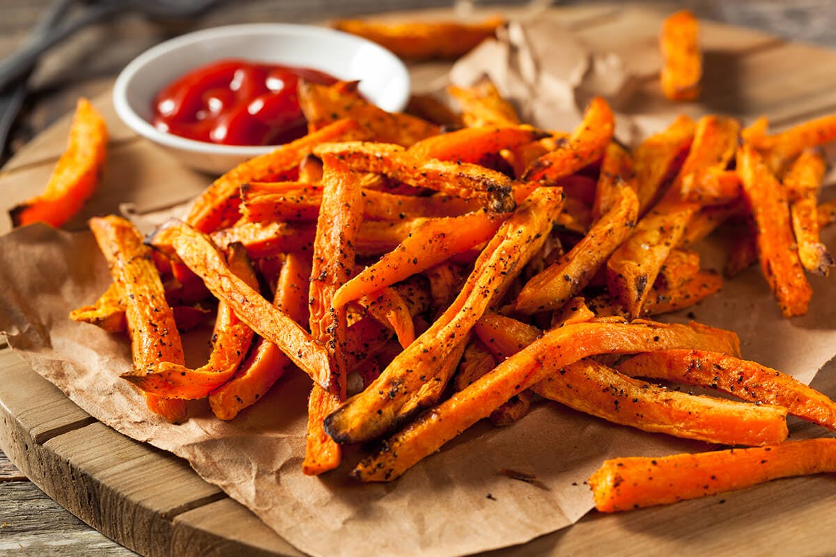 A platter of baked sweet potato fries with a side cup of ketchup