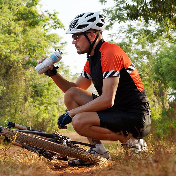 Man drinking water while crouching near bicycle.