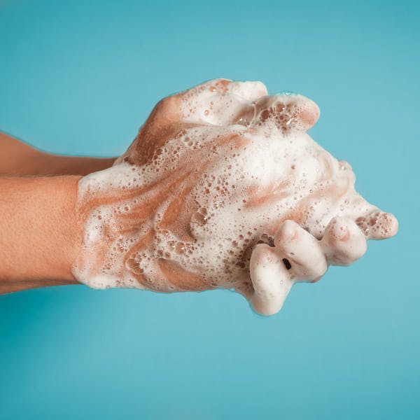 Close up of person washing hands against blue background.