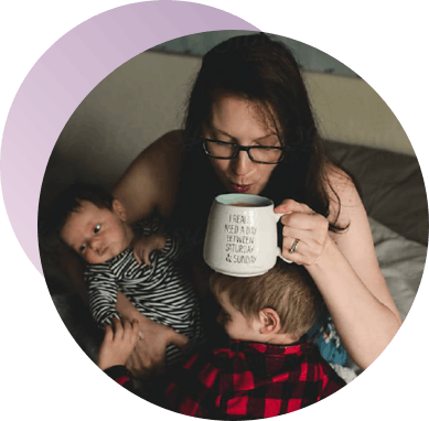 Woman sips coffee in bed while holding baby and toddler Woman sips coffee in bed while holding baby and toddler